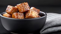 Crispy caramelized pork belly cubes glazed with sweet and savory sauce served in black ceramic bowl on dark background with gray linen napkin.
