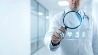 Male doctor in white coat holding magnifying glass with digital medical icons in modern hospital corridor for healthcare technology and diagnostic concepts.