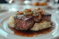 Grilled beef steak with caramelized onions and creamy mashed potatoes served on white plate with rich brown sauce in elegant restaurant setting.