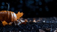 Orange pumpkin with autumn maple leaves on dark soil against blurred bokeh background, dramatic Halloween or fall harvest seasonal composition.
