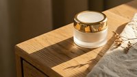 Luxury skincare cream jar with gold lid on wooden nightstand in warm sunlight, elegant beauty product for moisturizer or anti-aging cosmetic branding.