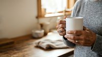 Senior woman holding white mug in cozy home interior with warm natural light, relaxation and comfort concept for lifestyle and wellness.