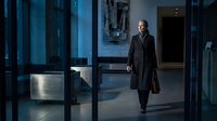 Professional businessman in dark suit walking through modern corporate office lobby with glass walls and contemporary architecture during evening hours.