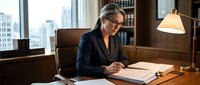 Professional mature businesswoman with glasses reviewing documents at wooden desk in modern office with city view and warm lighting for corporate presentations.