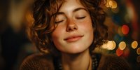 Young woman with curly red hair and freckles smiling with eyes closed in warm holiday lighting, creating peaceful festive atmosphere.