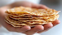 Stack of golden thin crepes or pancakes held in cupped hands ready for breakfast or dessert serving in kitchen cooking concept.