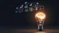 Glowing light bulb with brain filament and business icons floating above on dark background representing innovation and creative thinking in entrepreneurship.