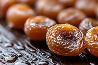 Macro shot of golden candied kumquats with glistening sugar coating on dark wooden surface, showing rich texture and natural sweetness of preserved citrus fruits.