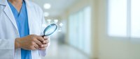 Male doctor in white coat holding magnifying glass with glowing medical icons in hospital corridor, healthcare research concept.