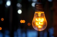 Glowing vintage light bulb with warm yellow illumination against blurred bokeh background creates atmospheric mood lighting effect.