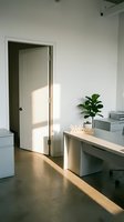 Minimalist modern office interior with sunlight streaming through a door, white desk, welcome sign, and green plant on concrete floor.