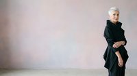 Senior woman with white hair wearing black blazer standing against neutral background, suitable for business, corporate, and professional lifestyle content.