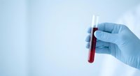 Medical professional in blue latex gloves holding blood sample test tube for laboratory analysis and diagnostic testing in clinical environment.