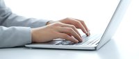 Hands of a young woman in a gray hoodie typing on a laptop keyboard, close-up side view on a white background.