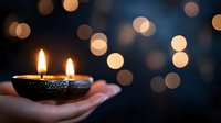 Traditional oil lamp with twin flames held in cupped hands against bokeh lights background for Diwali festival celebration and spiritual meditation ceremonies.