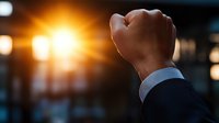 Raised fist of businessman against sunset light through window symbolizing success, determination, victory and achievement in corporate environment.