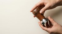 Male hands applying brown glass dropper bottle serum or essential oil on neutral beige background. Skincare routine and natural cosmetics concept.