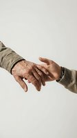 Elderly and young hands reaching toward each other in caring gesture representing intergenerational support and family connection on neutral background.