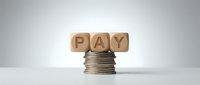 Wooden blocks spelling PAY balanced on top of stacked coins, representing salary, wages, compensation, and financial transactions for business and commerce concepts.
