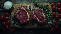 Raw ribeye steaks on wooden cutting board with fresh rosemary sprigs, cherry tomatoes and sea salt, dark moody food photography for restaurant menu or cooking blog.