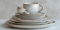 Handmade ceramic dinnerware set with speckled glaze finish featuring plates, bowls and cup in neutral beige tones for modern kitchen and dining decor.