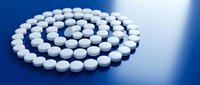 White pharmaceutical pills arranged in spiral pattern on blue background for medical healthcare and medication concepts.
