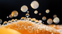 Macro photography of water drops on orange surface with bokeh effect creating artistic reflections and spherical patterns in black background.