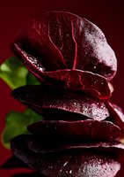 Fresh wet red cabbage leaves stacked in artistic composition with water drops and visible veins on dark background, dramatic lighting highlights texture.