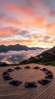 Meditation cushions arranged in circle on wooden deck overlooking mountain valley with clouds at sunrise for wellness retreat and mindfulness practice.