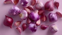 Fresh purple and pink garlic bulbs and cloves scattered on pink background, top view composition showing organic produce and culinary ingredients.
