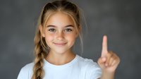 Young Caucasian girl with blonde braided hair and bright smile showing number one gesture with finger against gray background, wearing white t-shirt.