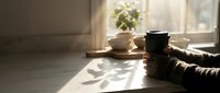 Cozy morning scene with coffee cups, plant and striped sweater on wooden table by sunny window creating warm atmospheric home interior.