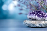 Purple amethyst crystal geode on stacked zen stones with lavender flowers creating peaceful spa meditation atmosphere for wellness and healing practices.