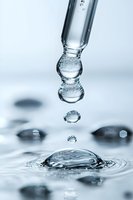 Macro photography of water drops falling and creating ripple effect on water surface, captured in high speed with crystal clear details in cool blue tones.