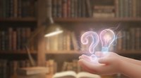 Hands holding glowing question mark and light bulb symbols in library setting representing curiosity, learning, knowledge discovery and problem solving.