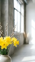 Yellow daffodils and pussy willow branches in ceramic vase by window create fresh spring home decor arrangement in bright modern interior space.