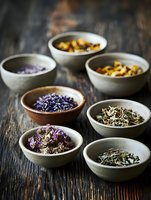 Assorted dried herbs, flowers and tea ingredients in ceramic bowls on rustic wooden background. Natural wellness and herbal medicine concept for spa and aromatherapy.