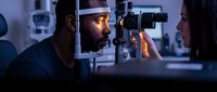 Male patient receiving comprehensive eye examination from female optometrist using advanced diagnostic equipment in modern clinic for vision care and health.