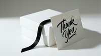 Elegant thank you card leaning against a white gift box with black ribbon, featuring stylish calligraphy lettering on light background.