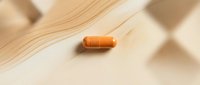 Orange capsule pill on wooden surface for healthcare and pharmaceutical supplement concepts.