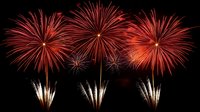 Spectacular red fireworks display against dark night sky with symmetrical bursts and white fountain effects creating dramatic celebration atmosphere.
