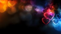 Glowing hearts with colorful bokeh effect on dark background create romantic atmosphere. Soft focus pink, blue and orange lights form dreamy valentine pattern.