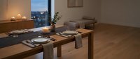 Modern dining room with wooden table set for two, warm candlelight, and city skyline view through large windows at dusk for home decor and interior design.