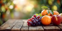 Fresh seasonal fruits including red grapes, orange, and apple arranged on rustic wooden table with warm natural lighting and blurred garden background.
