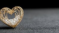 Golden wire heart-shaped frame with white pearls on textured dark surface for romantic jewelry design and Valentine's Day decorations.
