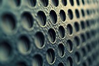 Close-up macro shot of metallic mesh or grid with circular holes creating abstract industrial pattern in dark teal and silver tones, selective focus effect.