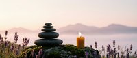 Zen stone stack with burning candle surrounded by lavender flowers at sunset creating peaceful meditation atmosphere for wellness and relaxation practices.