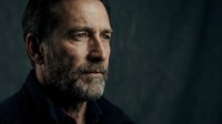 Middle-aged man with full beard and dark hair, Caucasian ethnicity, wearing black clothing against dark background. Serious, contemplative expression suitable for corporate, editorial, and dramatic storytelling projects.