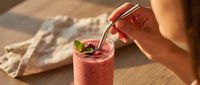 Person stirring refreshing berry smoothie with mint garnish on wooden table, ideal for beverage and wellness content.