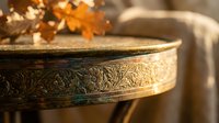 Ornate brass singing bowl with intricate floral engravings sits on wooden surface with autumn maple leaves and warm bokeh lights creating peaceful meditation atmosphere.